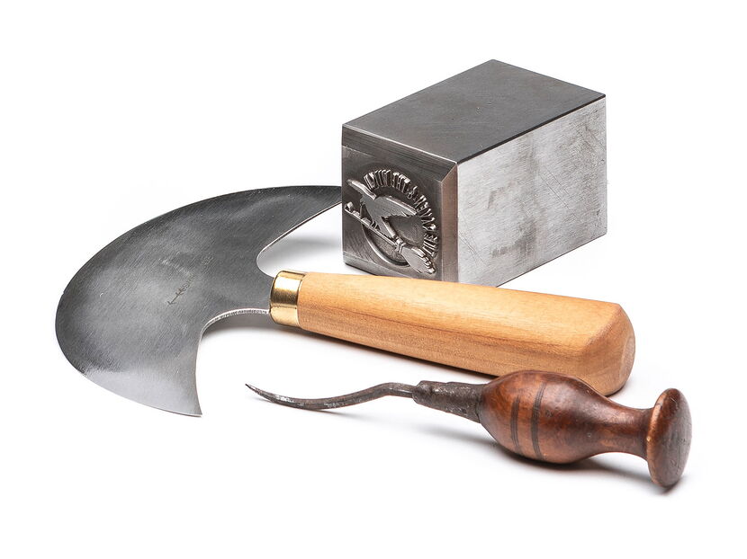 Werbefotografie: Handsichel, Lochnadel mit dunkelbraunem Griff und Metallprägestempel auf weissem Hintergrund