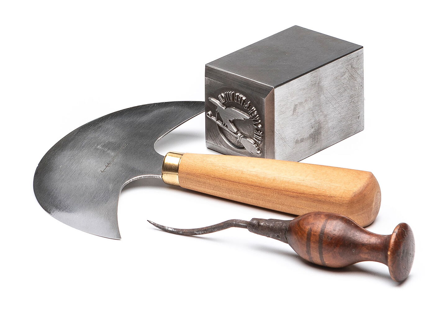 Werbefotografie: Handsichel, Lochnadel mit dunkelbraunem Griff und Metallprägestempel auf weissem Hintergrund