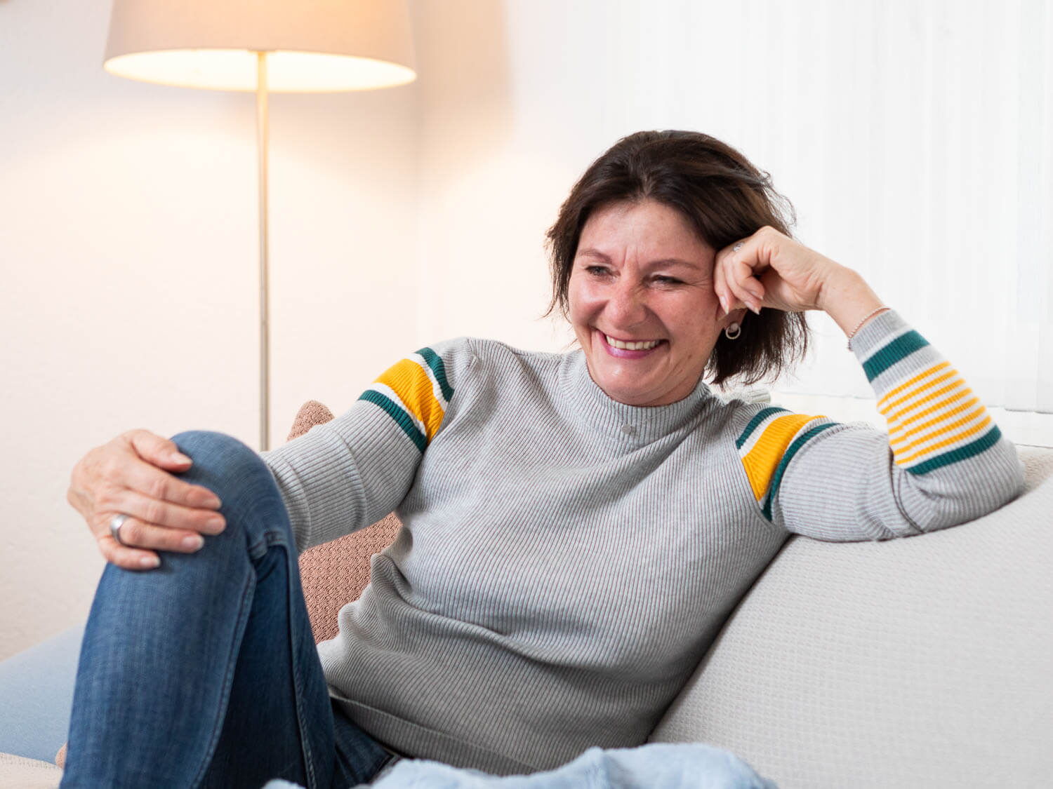 portraitfotograf luzern: Foto einer lachenden Frau auf hellgrauem Sofa